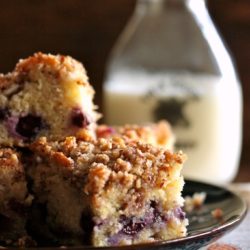 A square of Blueberry Pecan Crumble Coffee Cake on a plate in front of a jar of milk