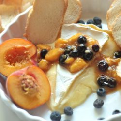 Baked Brie with Gingered Peach and Blueberry sauce and crostini in a white dish