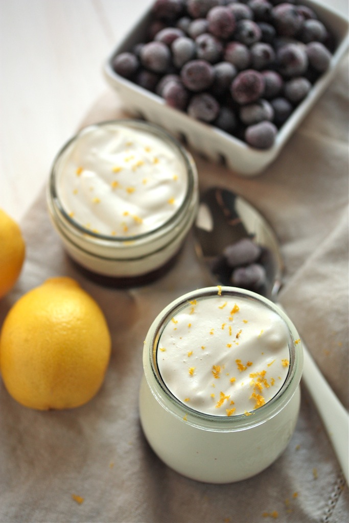 Two jars of lemon mousse with spoon, pint of blueberries, and lemons
