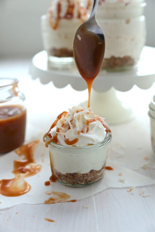 no bake coconut samoas cheeseccake on a white background with caramel dripping from a spoon