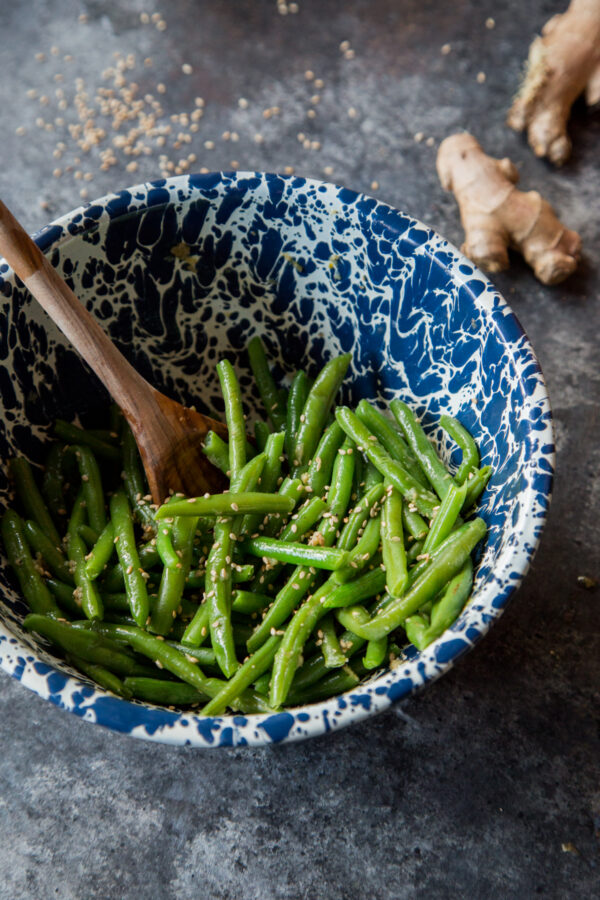 Garlic sesame green beans in a blue and white bowl with ginger