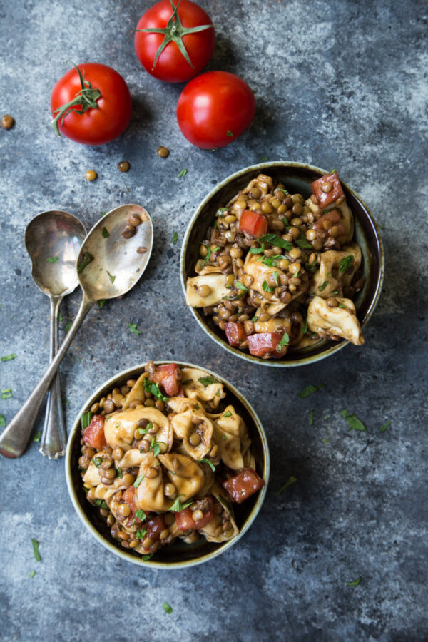 Lentil Tortellini Salad with Balsamic Vinaigrette overhead shot on a black and gray background with two bowls and red tomatoes