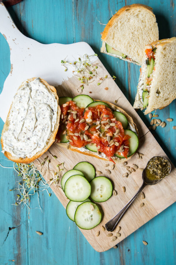Pesto Tomato Cucumber Sandwich overhead shot on a cutting board and blue background