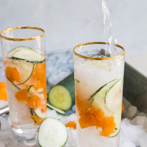 Apricot cucumber gin fizz in two glasses being poured