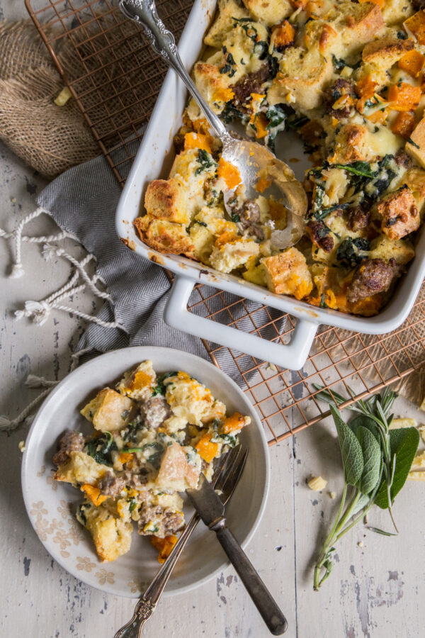 Savory Butternut Squash and Gruyere Strata with serving spoons in a white dish