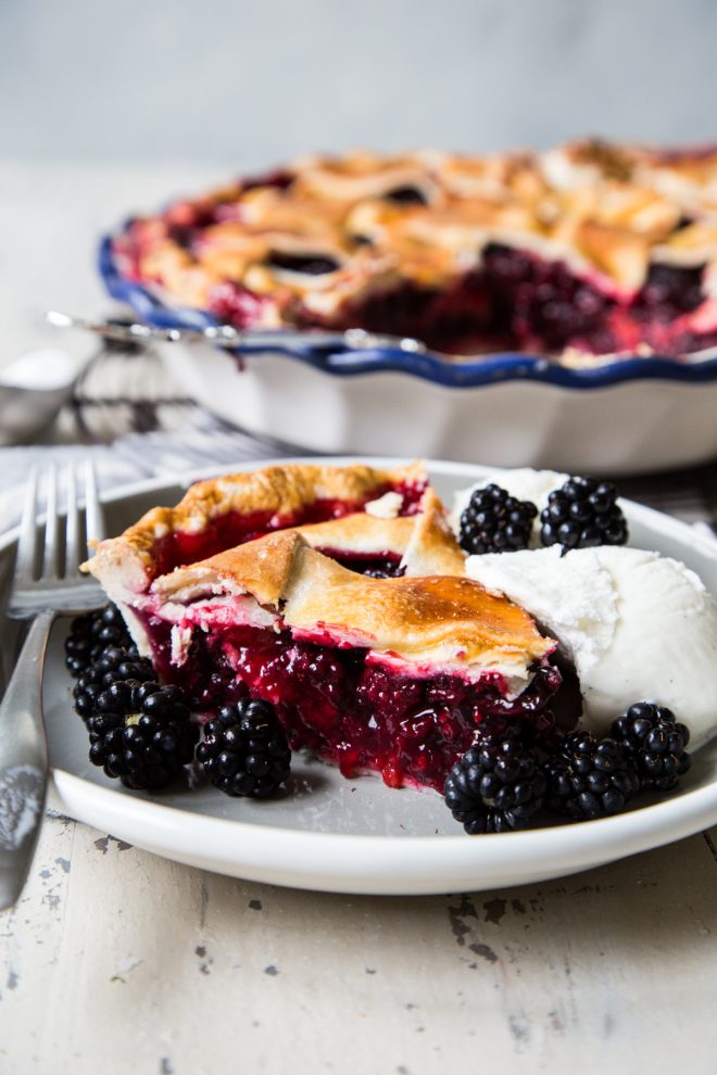 Blackberry pie slice with fresh blackberries surrounding it with a scoop of vanilla ice cream