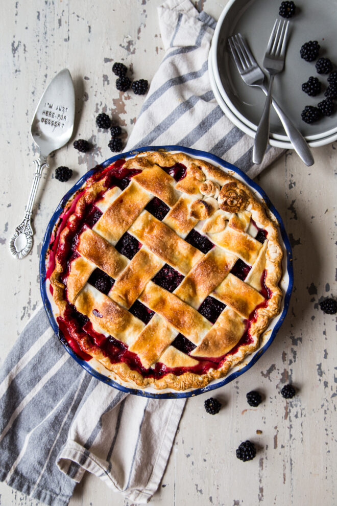 Blackberry pie slice with fresh blackberries surrounding it.