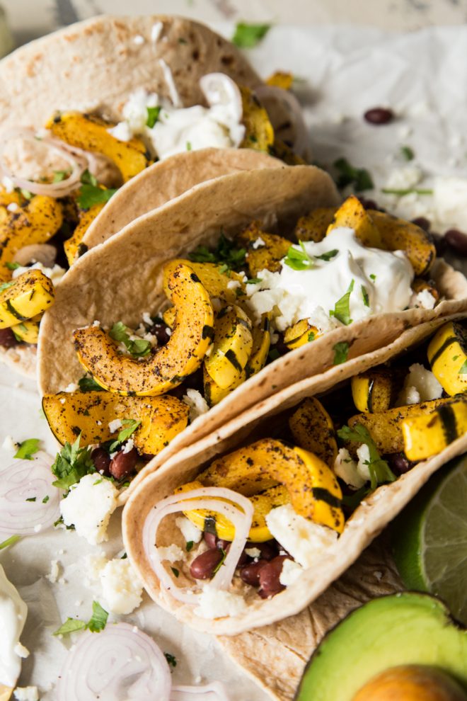 three delicata squash soft tacos on parchment paper with an avocado