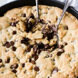 overhead photo of brown butter chocolate chip skillet cookie with two spoons in the middle