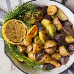 Roasted baby potatoes in white enamel skillet with lemon slice and fresh dill