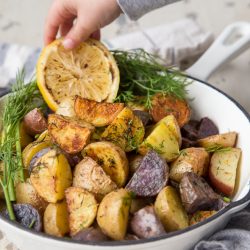 Toddler hand reaching for slice of lemon in skillet of roasted potatoes with dill