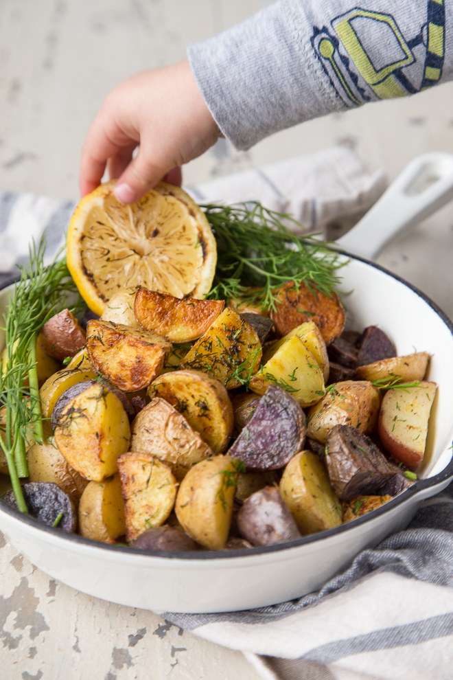 Toddler hand reaching for slice of lemon in skillet of roasted potatoes with dill