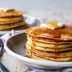 Close-up of a stack of Banana Sourdough Pancakes on a plate with butter and syrup