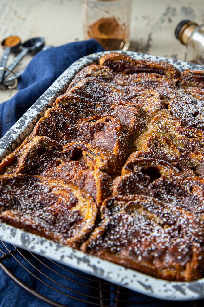 baked french toast in a gray and white speckled dish on a brown cooling rack, on a blue fabric napkin
