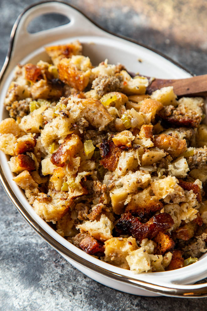 Slow cooker apple sausage stuffing in a white serving dish on a dark background