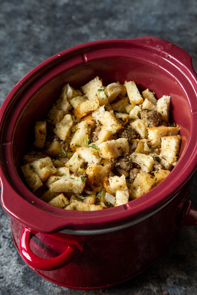 Slow cooker apple sausage stuffing in a red slow cooker with parsley garnish