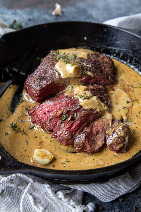 Cast Iron Bavette Steak with Whiskey Garlic Cream Sauce sliced thinly shot in the pan with black utensils