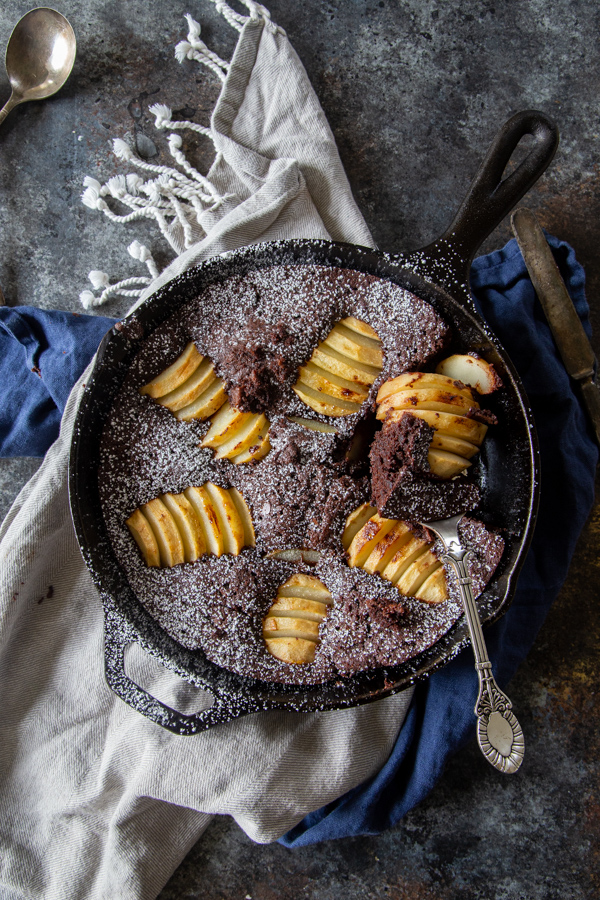 Chocolate chai and pear skillet cake in a cast iron skillet on a gray and blue napkin shot overhead
