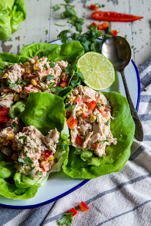 Whole30 chipotle chicken salad on lettuce leaves and a white distressed background with lime and bell pepper