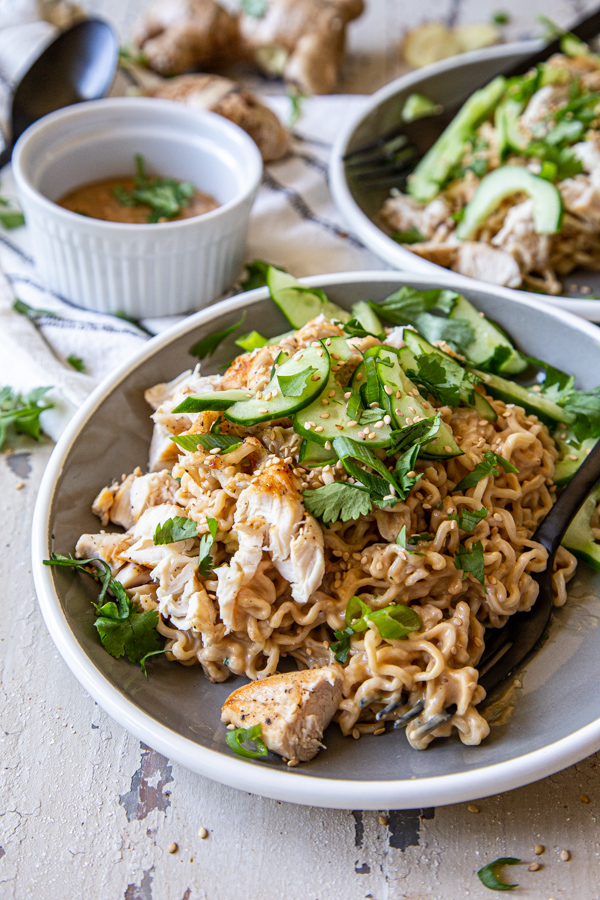 Cold Peanut Noodles with Chicken close up with cilantro and cucumbers on gray and white plates