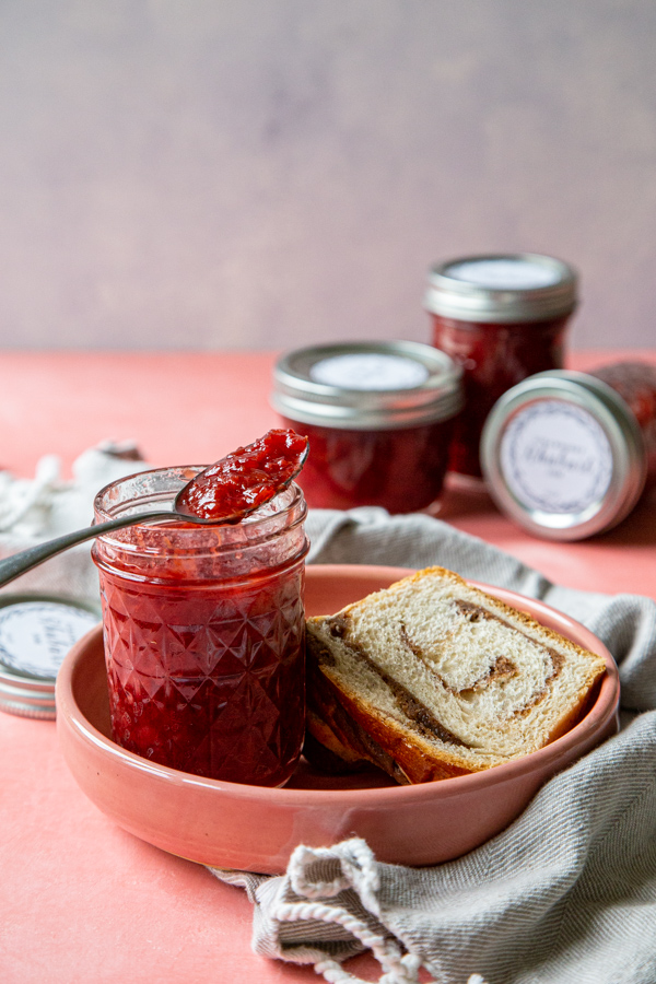 strawberry rhubarb jam overhead on a pink background and pink plate with jam jars in the background