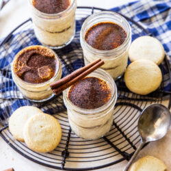 4 jars of tiramisu on wire rack with shortbread cookies, cinnamon stick, and spoons scattered in background