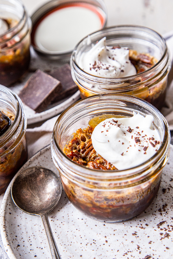 Pecan pies in glass jars pictured on plates with spoon and squares of chocolate