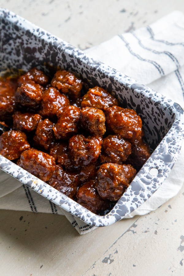 Slow cooker chipotle apricot meatballs in a gray and white loaf pan for serving on a white distressed table and napkin