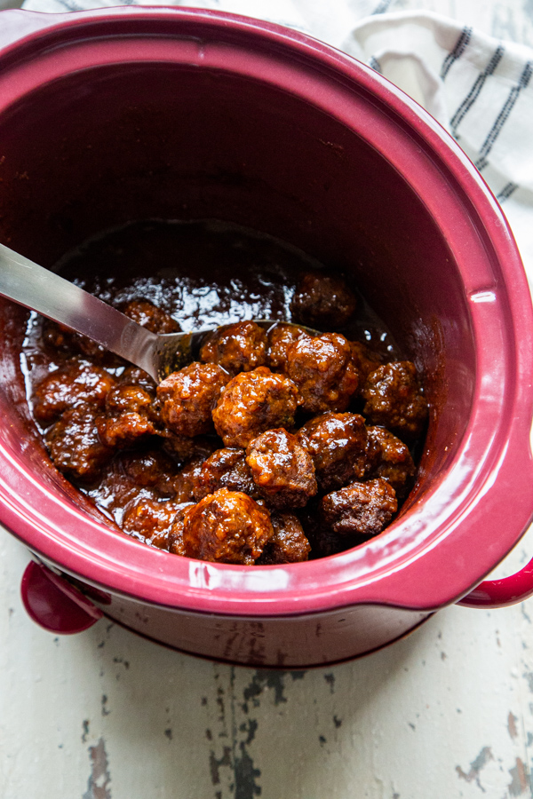 Slow cooker chipotle apricot meatballs in a red slow cooker crock pot on a white distressed table