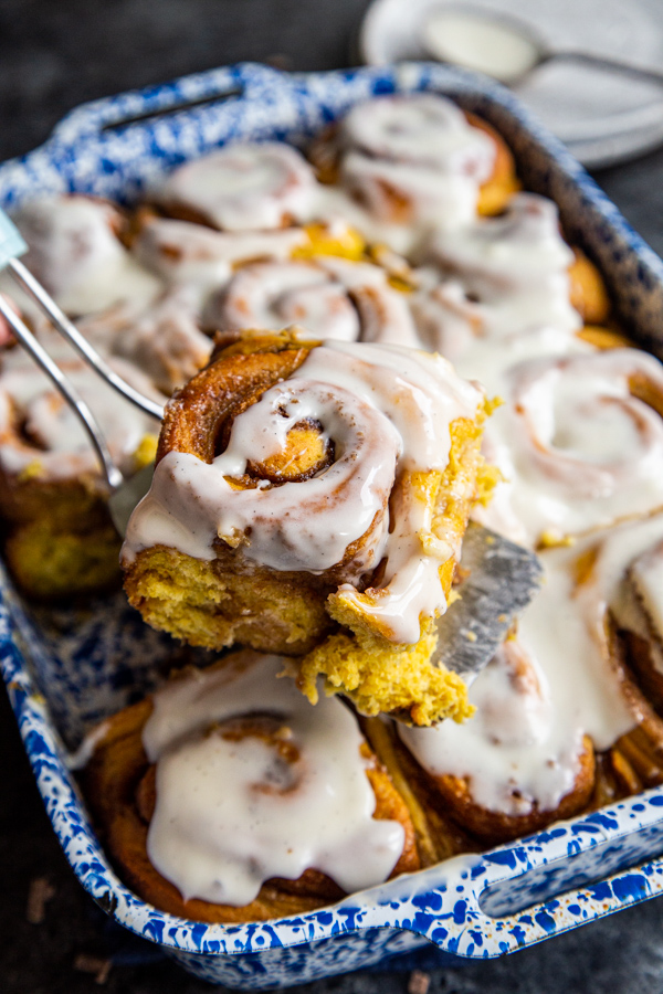 Frosted cinnamon roll being lifted from baking dish